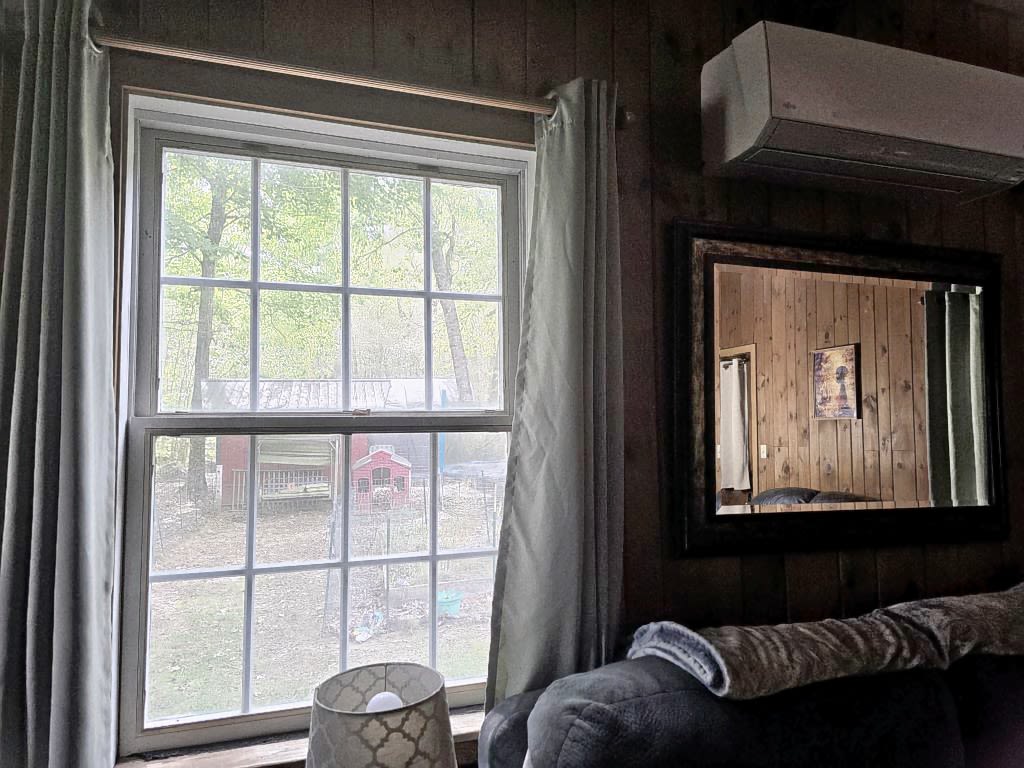 A muted view through another grid pane of glass, glimpsing into the bright outdoors. Reflected in the mirror hangs a lit painting of a woman with an umbrella walking freely in an autumn forest.