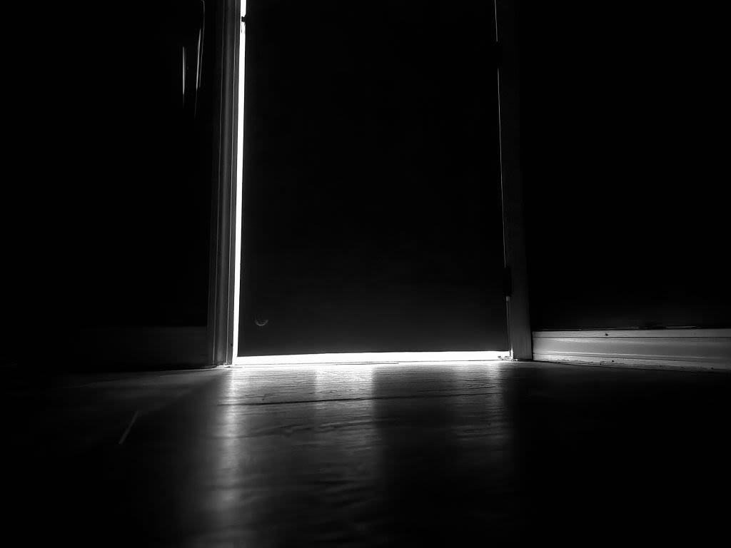 The rim of a cracked bedroom door, with the light from the hallway beyond roaring to break inside, though I often kept it shut out.